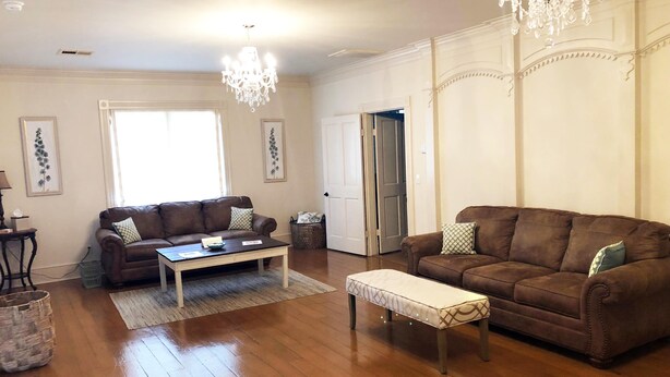 A living room with a brown leather sofa, a matching ottoman, a coffee table, and a chandelier. - Marie Celeste Creole Country Cottage (Destrehan)