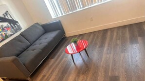 Een woonkamer met een donkergrijze bank, een rode glazen salontafel met een plant, en een houten vloer.