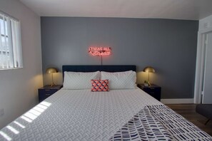 A neatly made bed with a patterned bedspread, two bedside lamps, and a neon sign on the wall.