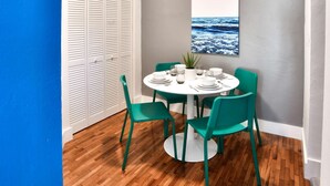 Un coin repas avec une table ronde, quatre chaises vertes, des assiettes blanches et une plante en pot.