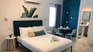 Une chambre d’hôtel avec un lit, une petite table avec des chaises, un lavabo et une fenêtre avec des rideaux.