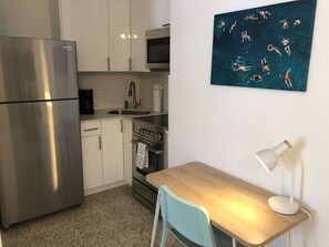 A compact kitchen with a refrigerator, stove, microwave, and sink. There's a small table with a chair and a wall-mounted lamp. - ✨ New Studio plus FREE parking fee (Miami)