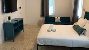 A hotel room with a bed, a TV, a small table, and a window with curtains.