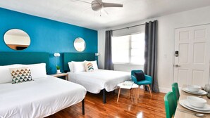 A hotel room with two beds, a ceiling fan, a window with curtains, a dining table with chairs, and a door. - ✨ New Studio Plus Free Parking (Miami)
