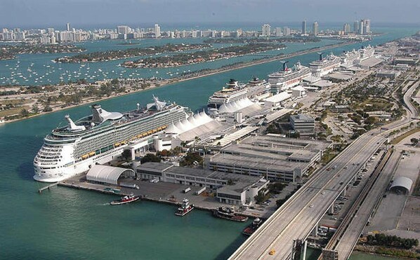 A large cruise ship docked at a port with multiple terminals, connected by a bridge, and surrounded by a cityscape with a marina in the background. - ✨ New Studio Plus Free Parking (Miami)