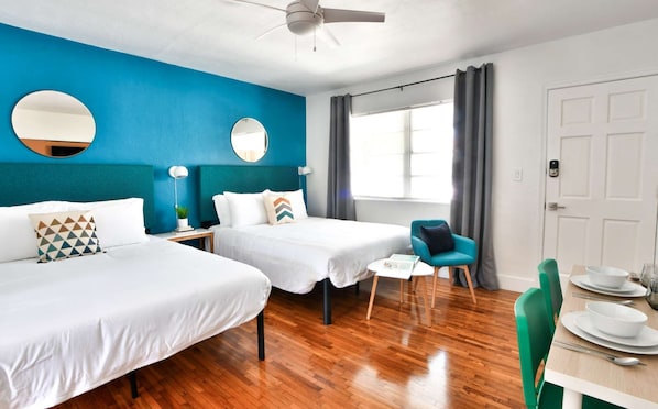 Two single beds with white linens, a round mirror, and a ceiling fan are featured in this stylish room.
