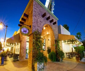 A building with a brick facade, arched entrance, outdoor seating area, and a sign with a vehicle logo. - ✨New Two Bedroom plus Free Parking (Miami)