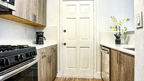 A compact kitchen with a stove, oven, and microwave. There is a white door and a small plant on the counter. - ✨ New Two Bedroom plus Free Parking (Miami)