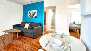 A modern living room with a grey sofa, a small round table, and a dining area with a white table set for two. - ✨ New Two Bedroom plus Free Parking (Miami)