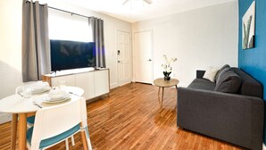 A modern living room with a grey sofa, a dining table with white chairs, and a small round table with a plant. - ✨ New Two Bedroom plus Free Parking (Miami)