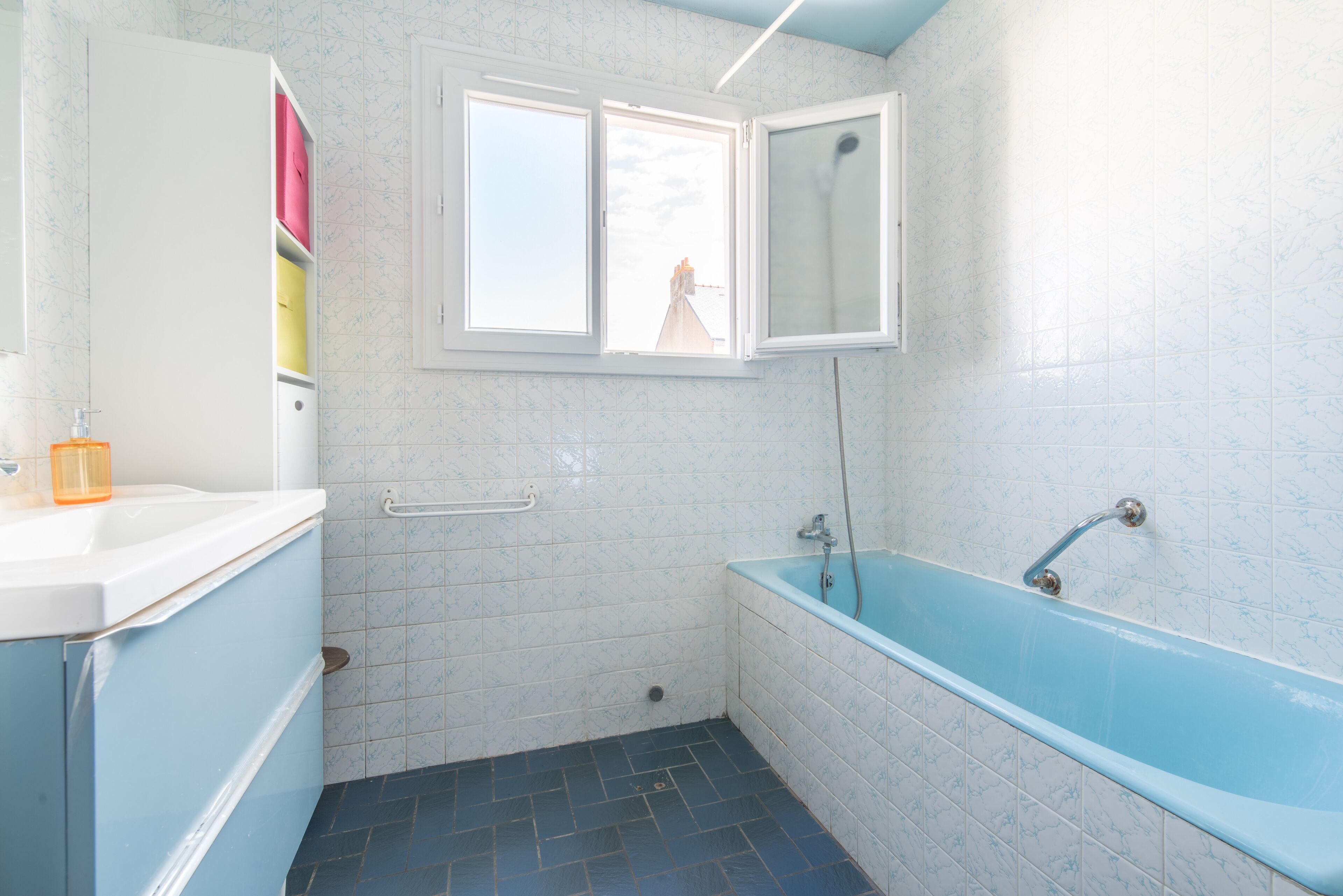 A bathroom with a bathtub, a window, and a white cabinet with pink and yellow items.