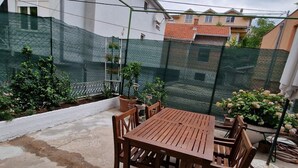 A patio with a wooden table and chairs, surrounded by a green mesh fence and potted plants. - Old bridge (Mostar)