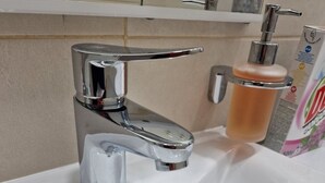 A bathroom sink with a chrome faucet, a soap dispenser, and a drain. - Old bridge (Mostar)