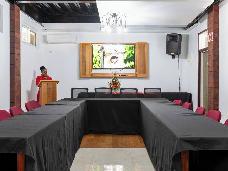 A conference room with a long table, red chairs, a podium, and a screen displaying an image.