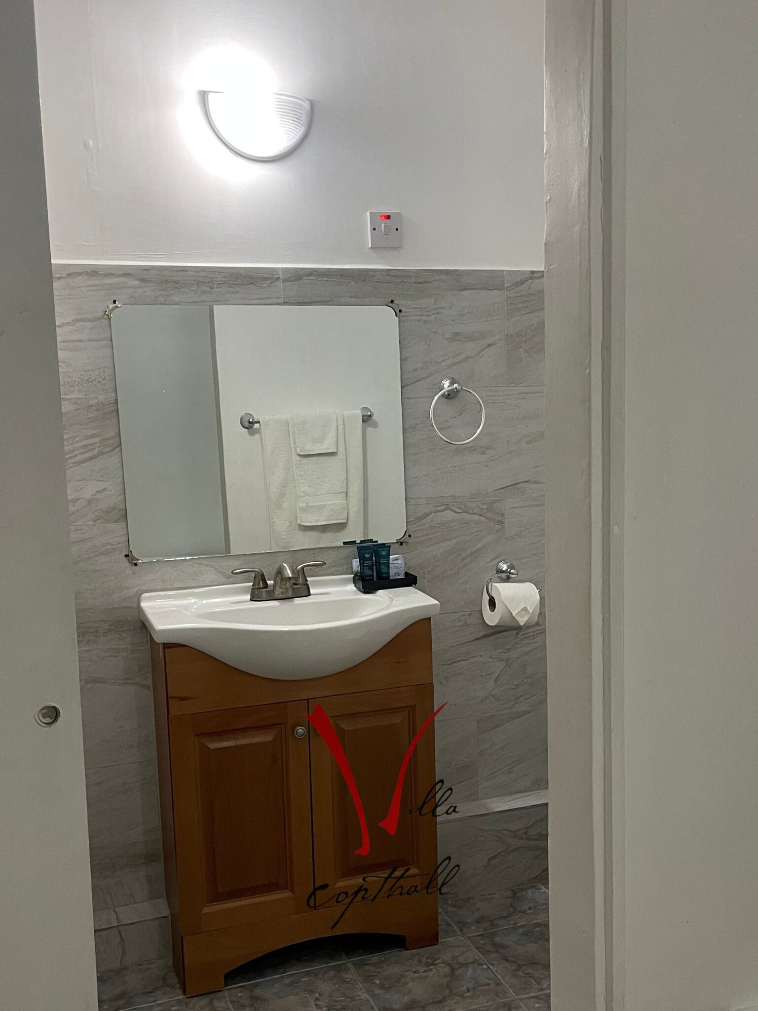 A bathroom with a white sink, wooden vanity, a mirror, a towel ring, and a toilet paper holder.
