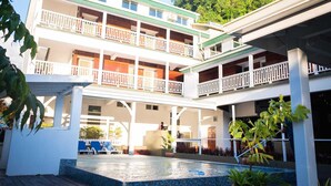 A multi-story hotel with a pool area, balconies, and a lush green backdrop.