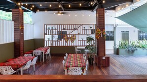 An outdoor dining area with wooden tables and chairs, string lights, and a view of a building in the background.