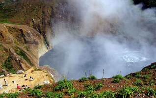 Una fuente termal natural con cascada, rodeada de terreno rocoso y vegetación escasa.