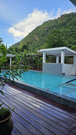 A swimming pool with a tiled edge, surrounded by a wooden deck and lush greenery.