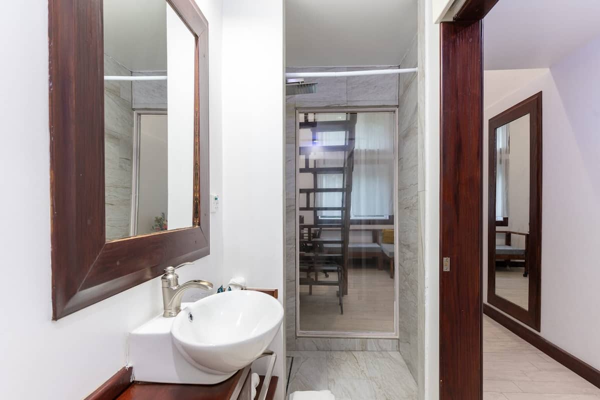 Un baño moderno con un espejo grande, lavamanos blanco y cabina de ducha de cristal.