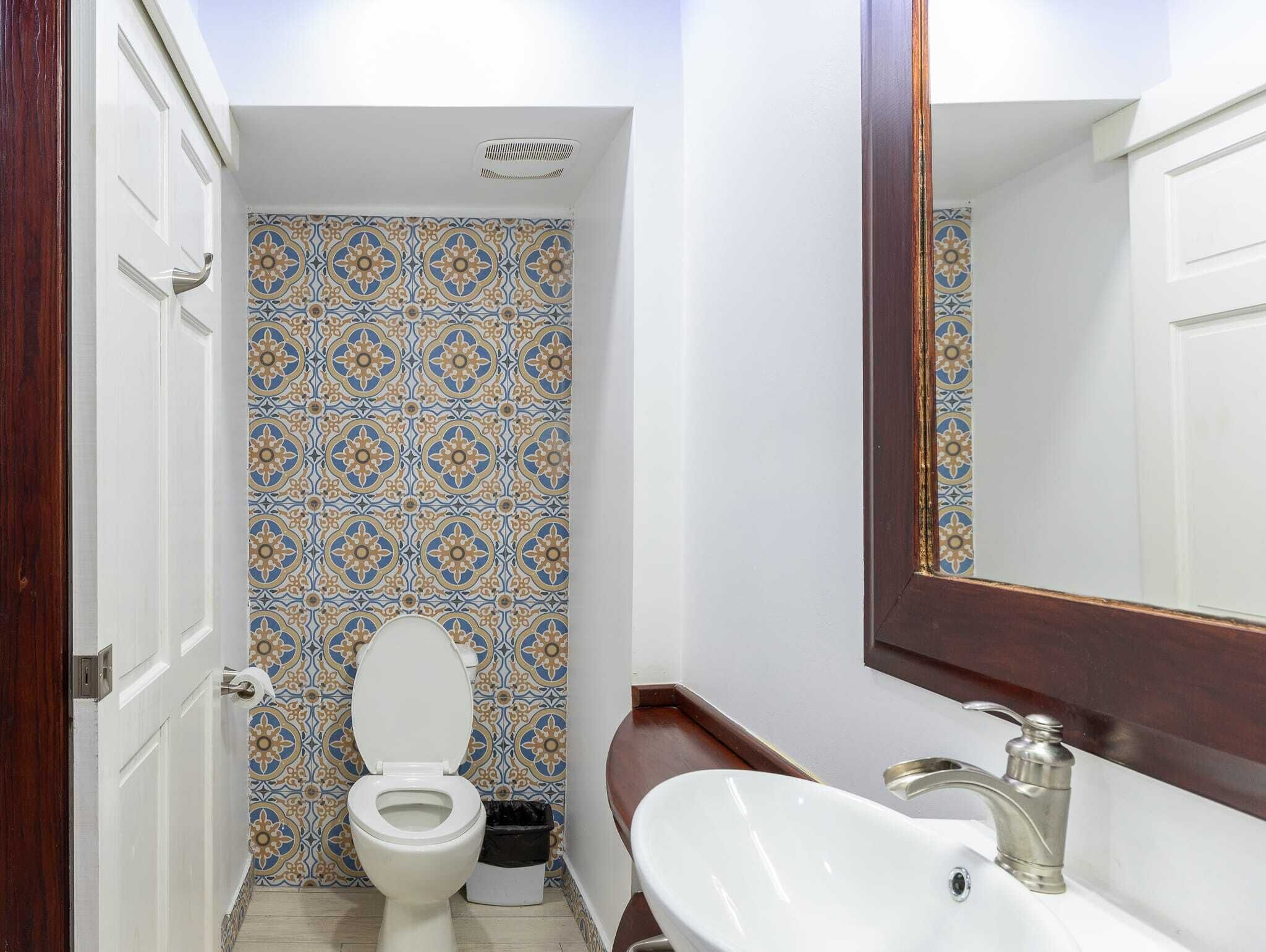 Un baño con pared de azulejos estampados, inodoro blanco, lavamanos con grifo moderno y espejo.