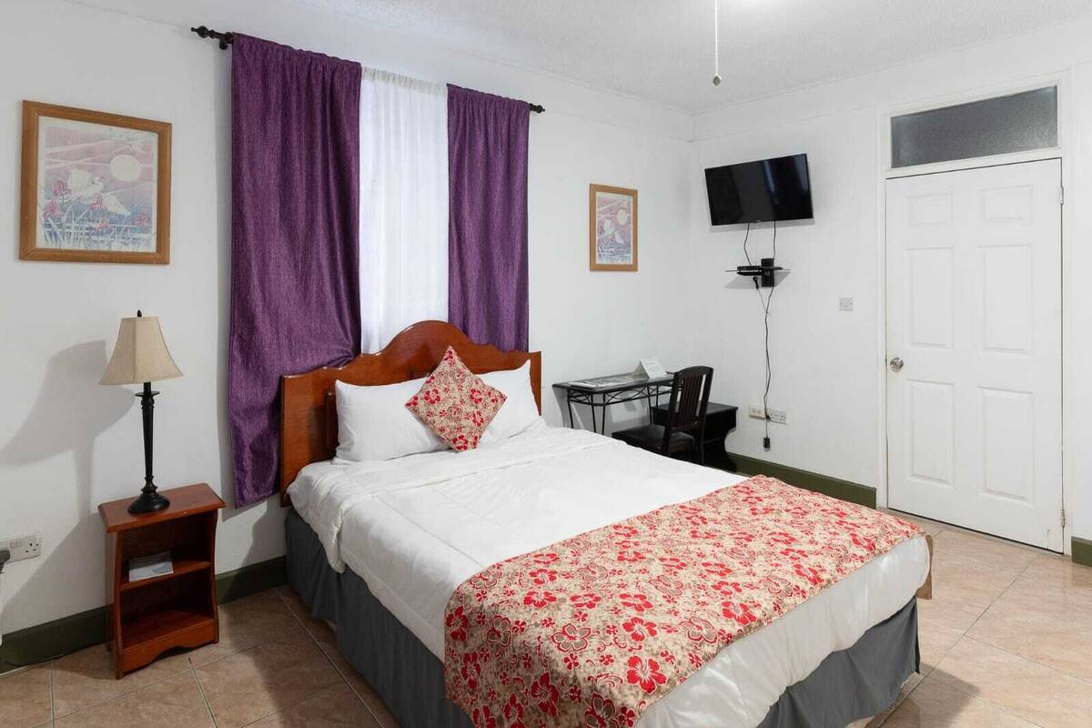 Un dormitorio con una cama, un escritorio, una silla, una lámpara y un televisor.