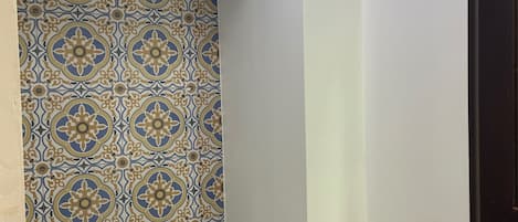 Un bagno con parete rivestita di piastrelle decorate, un WC bianco, uno scaffale in legno e un cartello con la scritta "Villa Opti hall".