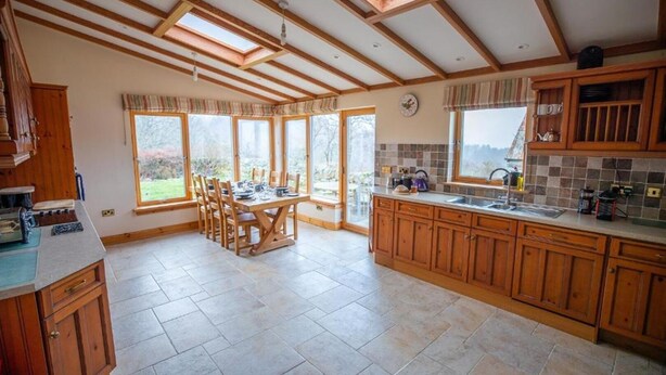 Una cocina amplia con armarios de madera, una zona de comedor con mesa y sillas, y ventanas grandes que ofrecen vistas al exterior.