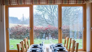 Mesa de comedor preparada para seis personas, con vistas a un jardín a través de amplios ventanales.