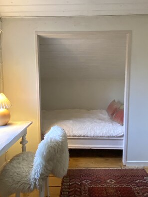 A room with a bed, a small table with a lamp, and a fluffy chair.
