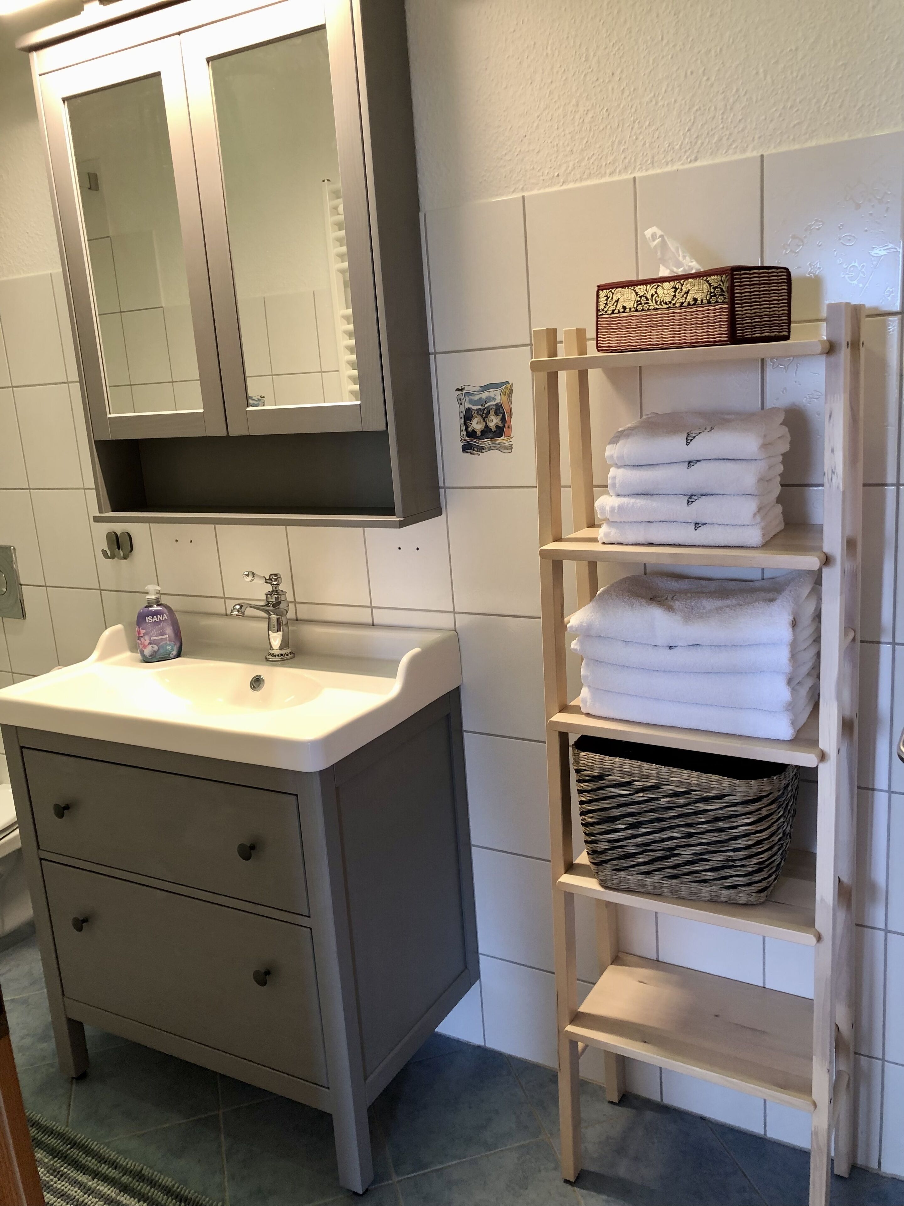 A bathroom with a sink, mirror, and wooden shelves holding towels and baskets.
