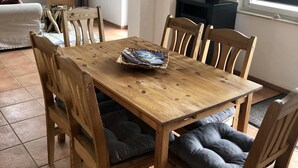 A dining area with a wooden table and chairs, a basket of magazines, and a television in the background. - Aalhaus Wustrow apartment to the meadow 900 m to the beach (Wustrow)