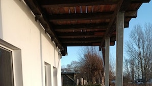 A covered walkway with a brick path leading to a white building with large windows. - Aalhaus Wustrow apartment to the meadow 900 m to the beach (Wustrow)