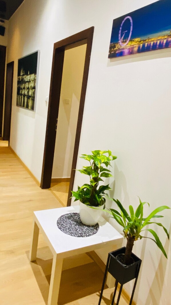 Un pasillo con suelo de madera, una mesa blanca con planta en maceta y un cuadro en la pared.