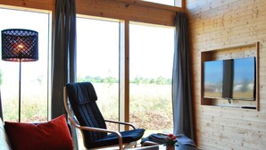 A cozy room with a large window, a chair, a sofa, a table, and a TV mounted on the wall. - Wooden holiday home "Feldrain" on the Baltic Sea - Sauna - 500m to the Baltic Sea beach - Wlan (Zierow)