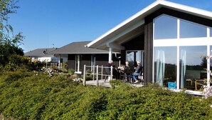 A modern house with a large glass window and a covered outdoor seating area. - Wooden holiday home "Feldrain" on the Baltic Sea - Sauna - 500m to the Baltic Sea beach - Wlan (Zierow)