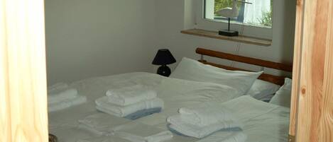 A neatly made bed with white linens and towels, a bedside lamp, and a window with a view of greenery.
