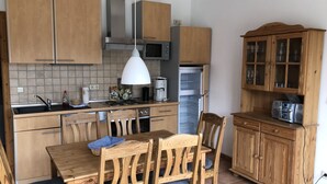Una cocina compacta con armarios de madera, microondas, refrigerador y un comedor con mesa y sillas.