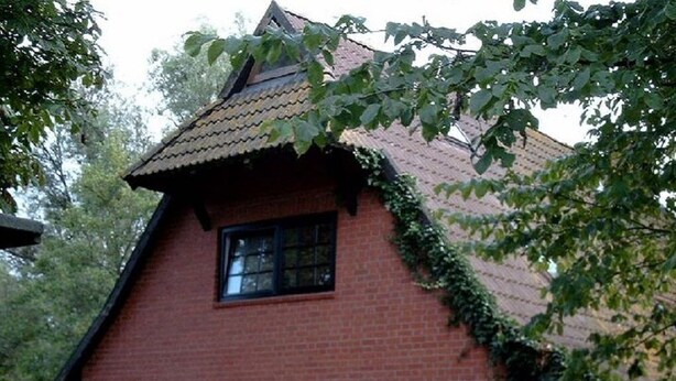 Una casa tradicional de ladrillo con techo a dos aguas, grandes puertas de garaje de madera y una ventana pequeña.