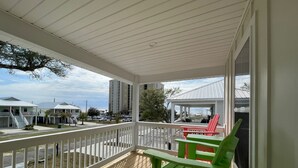 A covered porch with a wooden deck, white railing, and green and red Adirondack chairs. - Brand new home, 1 block from Beach (Gulfport)