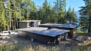 A modern cabin with a flat roof, surrounded by tall trees and a clear sky. - Amazing New 5 Bed Home next to the Columbia River. Sleeps 10 adults & 6 Kids (Stevenson)