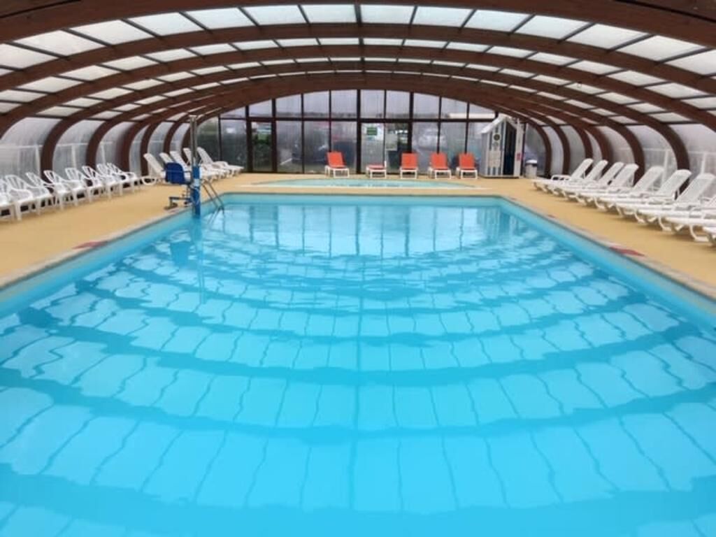 An indoor swimming pool with a clear view of the pool area, surrounded by lounge chairs and a covered roof structure.