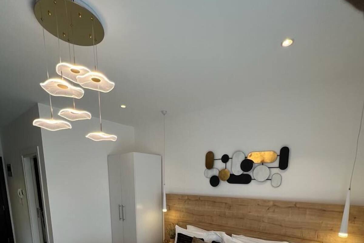 A modern bedroom with a large bed, a wooden headboard, a wall art piece, and a hanging light fixture.