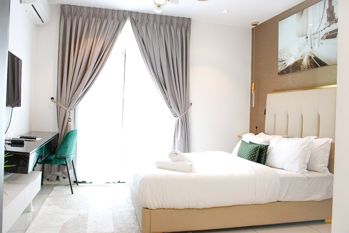 A hotel room with a bed, a desk, a chair, and a large window with curtains.