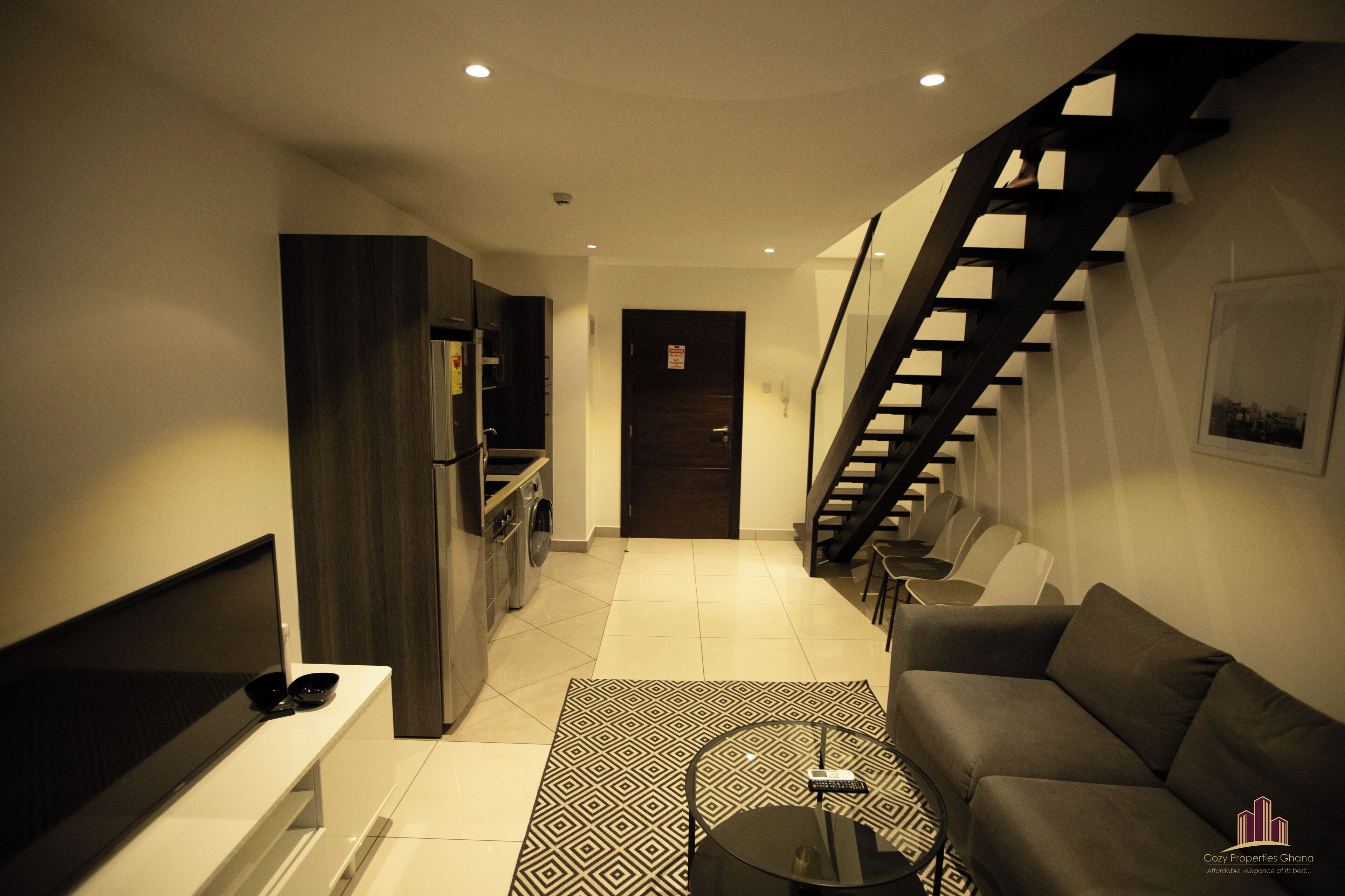 A modern living room with a sofa, a coffee table, and a TV. There is a staircase leading to another level.