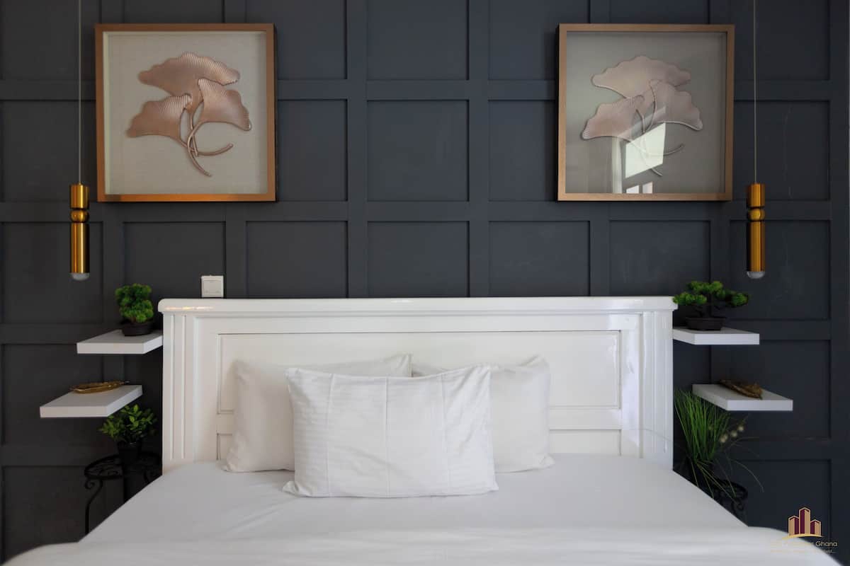 A neatly arranged bedroom with a white bed, two framed wall art pieces, and small shelves with plants.