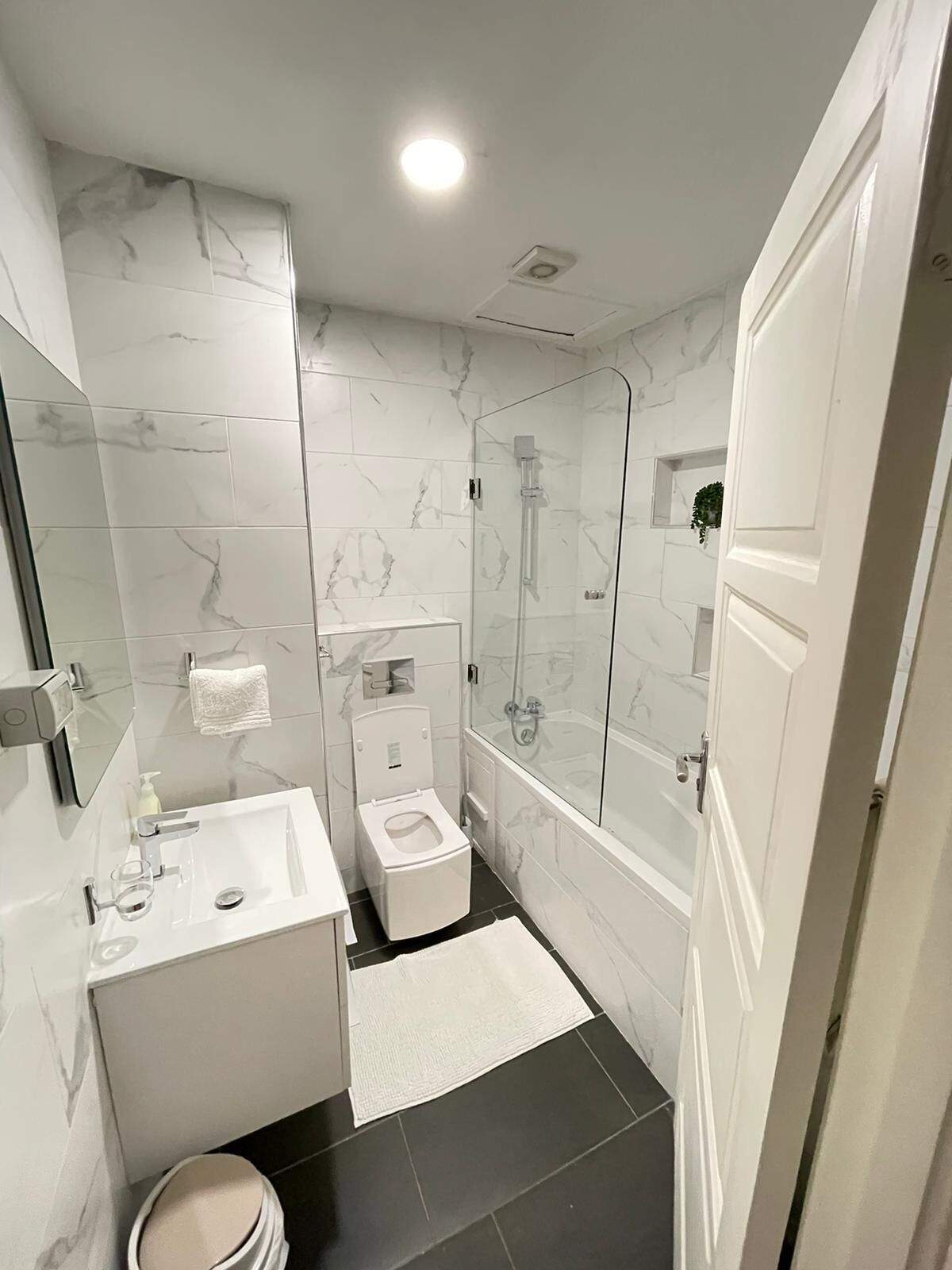 Une salle de bain moderne avec une douche à parois de verre, des toilettes blanches et un meuble-lavabo avec un miroir.