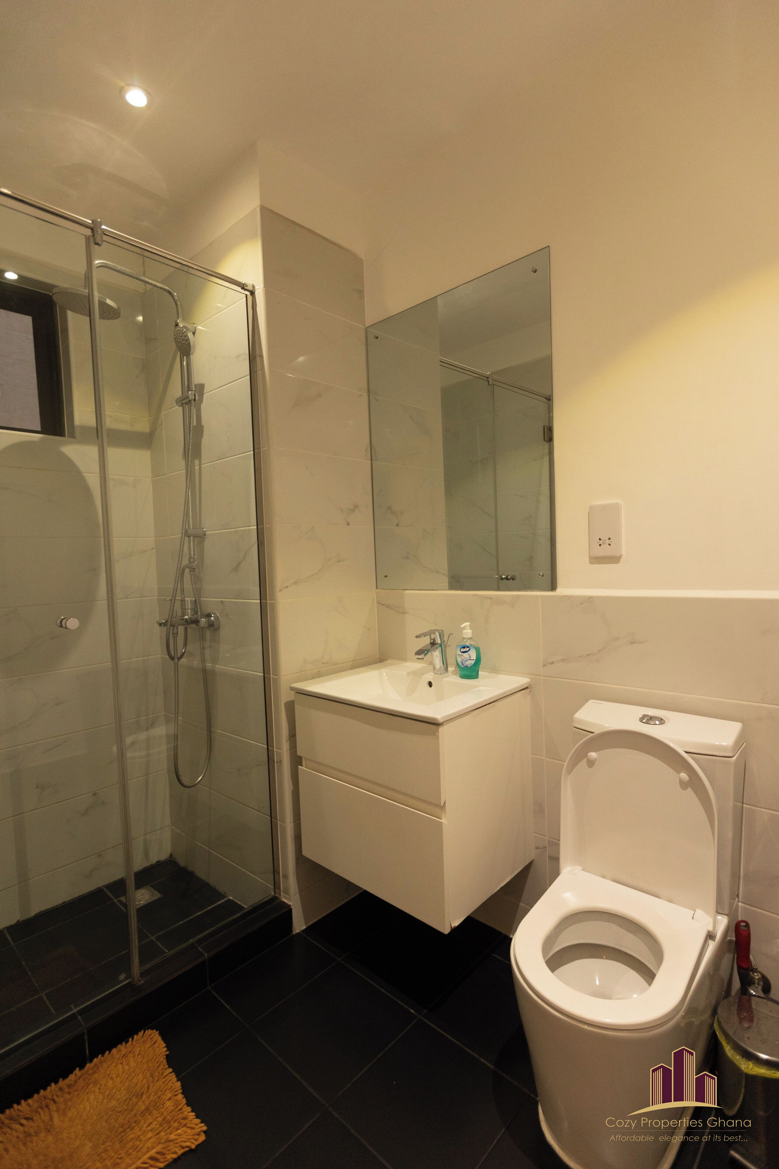 A modern bathroom with a glass-enclosed shower, a white sink, and a toilet.