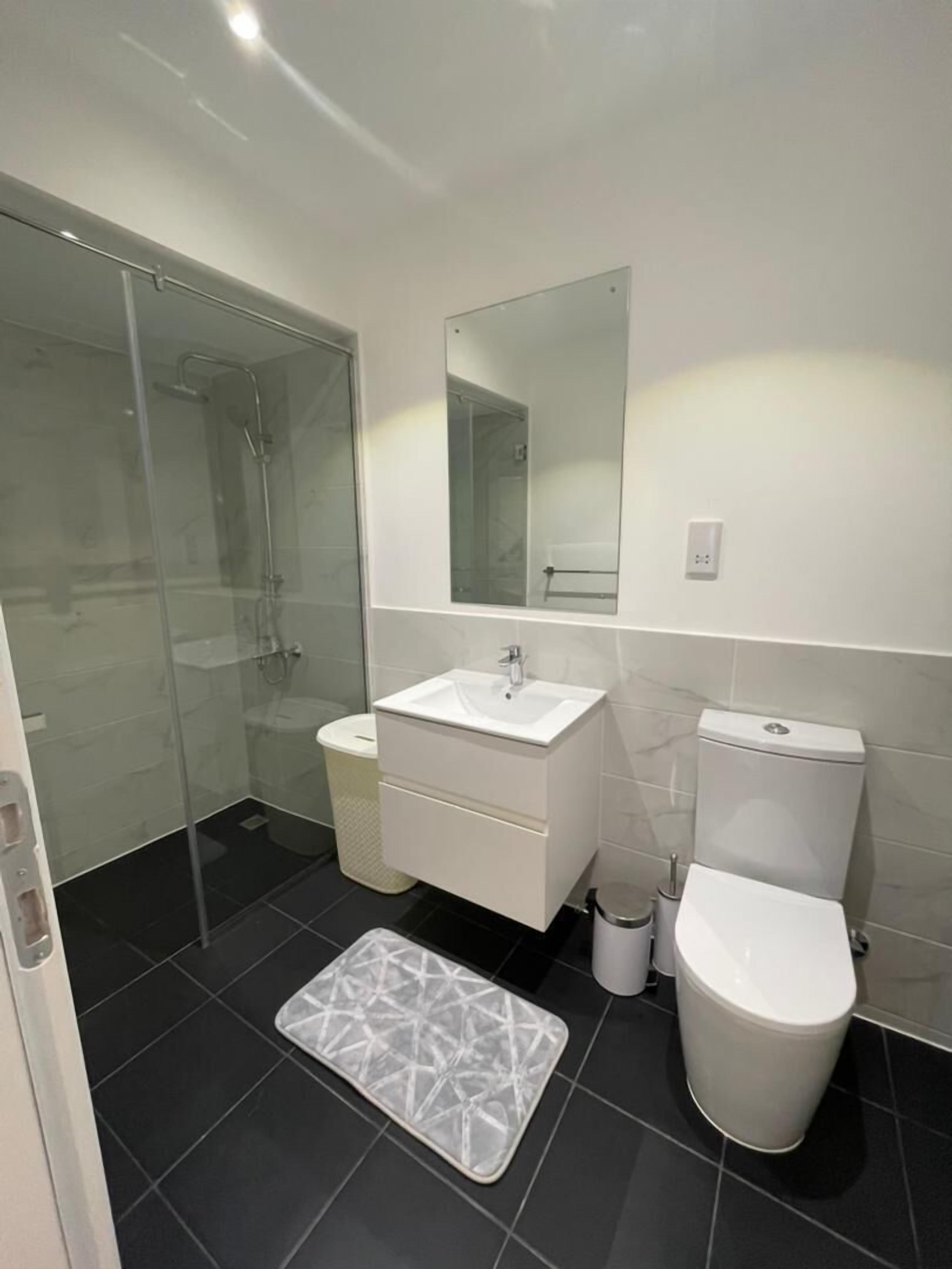 A modern bathroom with a glass shower enclosure, a white sink, and a toilet.