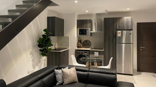 Una cocina moderna con electrodomésticos de acero inoxidable, un comedor con mesa de vidrio y un sofá de cuero negro.